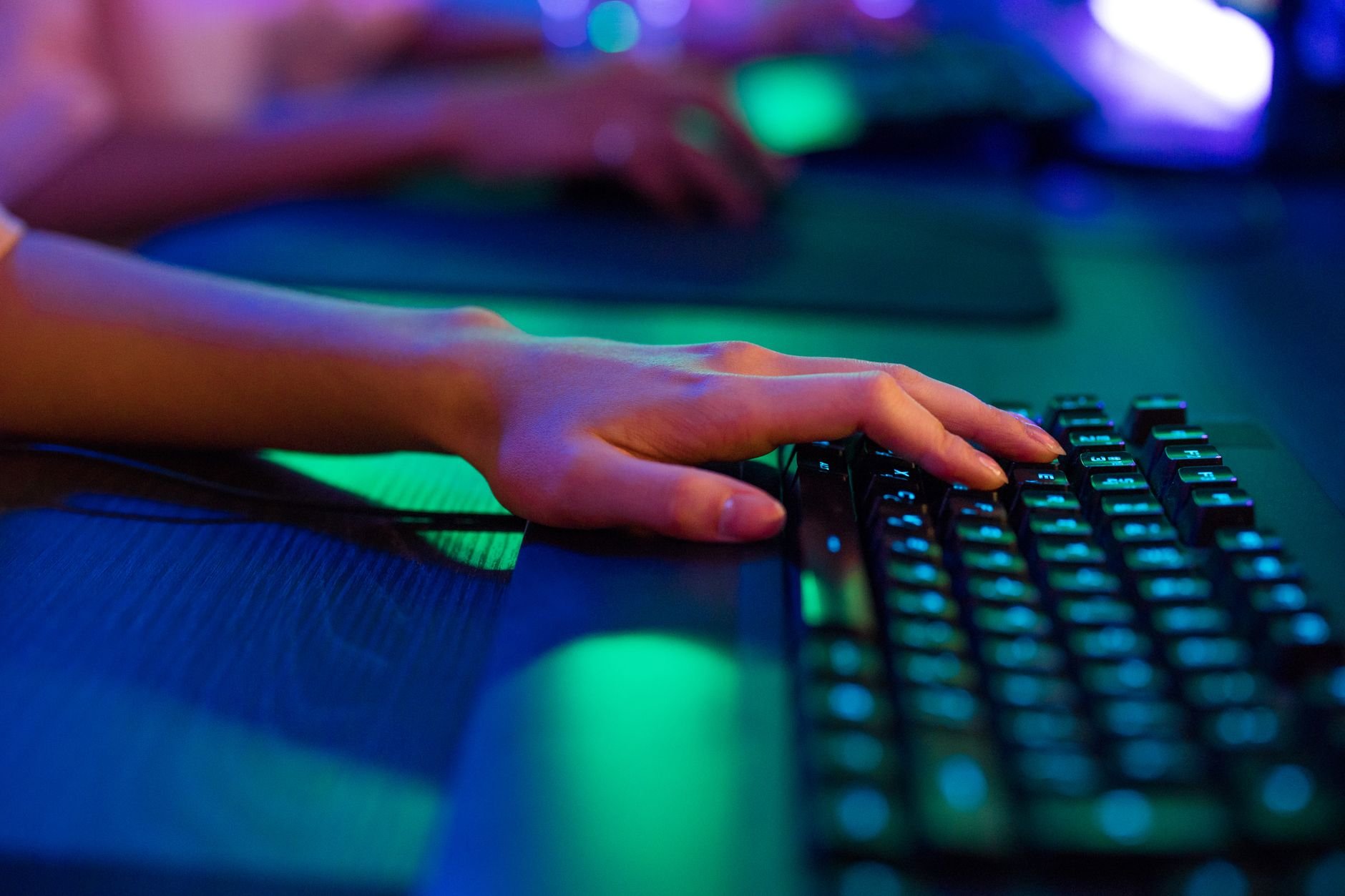 A close-up of a person's hand typing on a keyboard, illuminated by neon lights — focused and in the zone